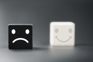 Unhappiness, dissatisfaction and negative emotions. Customer dislike, bad service quality. Negative feedback or evaluation. Sad face in black wood block and blur of the smile face in white wood block