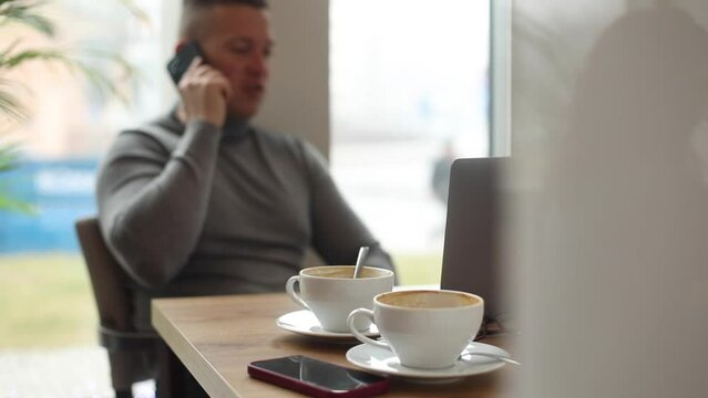 Video of sporty businessman having cream coffee phoning someone near expensive grey macbook on table in office