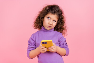 Photo of doubtful unsure little child dressed pullover typing apple samsung device looking empty space isolated pink color background