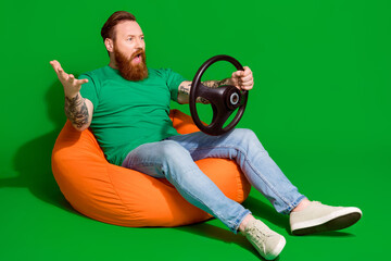 Full length photo of stressed angry man wear t-shirt sitting bean bag riding auto empty space isolated green color background