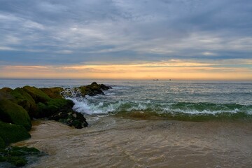 Scenic view of ocean waves crashing against mossy rocks at Sandy Hook, New Jersey at sunrise