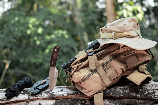 Equipment for survival bucket hat backpack hiking knife camping flashlight resting on wooden timber in the background is a forest