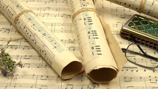 Rolled up sheets music, old harmonica and vintage glasses lie on the various old sheets music