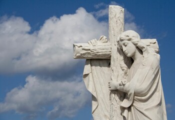 Beautiful white sculpture of an angel embracing a cross against a cloudy sky at Colon cemetery