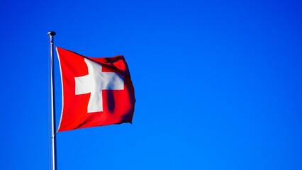 Waving flag of Switzerland around a pole against a clear blue sky