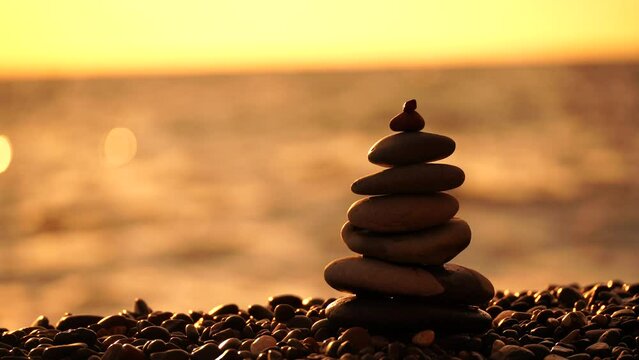 Balanced rock pyramid on pebbles beach. Golden sea bokeh on background. Selective focus, zen stones on sea beach, meditation, spa, harmony, calm, balance concept.