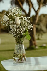 Vertical shot of a glass vase with blooming white flowers on an outdoor table