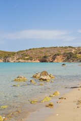 Vertical shot of rocks on the sea near the beach and a cliff in the background under blue sky