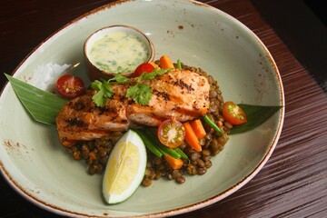 Closeup of delicious roasted salmon and lentil dish next to a sauce on a plate in a restaurant