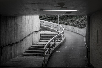 Grey drone shot of an asphalt road and stairs in underground tunnel