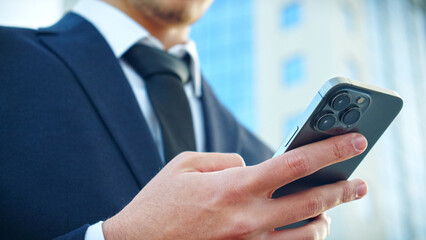 Businessman is typing text messages on mobile phone sitting in the park. Close up Male hands with smartphone, outdoors.  Human holds cell phone close up. Man holds mobile phone. Connection concept.