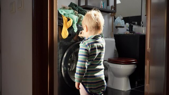 Little baby boy pressing knobs and buttons on working washing machine. Doing housework and chores, children education and development