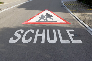 red and white attention school sign painted on concrete road. car drivers take care of pupils in traffic german text translation: school