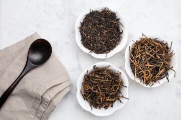Dry tea in a white bowls and empty wooden spoon on a white marble background. Dried tea leaves....