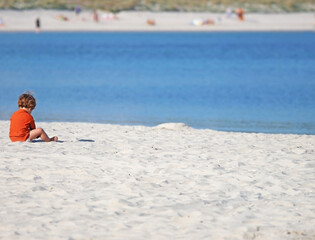 A small girl or boy playing alone with the sand on the beach. Space for text