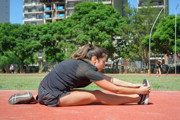 side view of young latin woman stretching legs and hips on the floor of the running track - obrazy, fototapety, plakaty