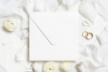 Square envelope near roses, white silk ribbons and wedding rings top view, wedding mockup