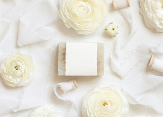 Handmade soap bar with blank label near cream roses and white ribbons top view, mockup