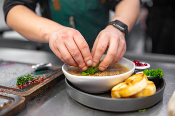 close up of male chef hand serving plate of soup at restaurant kitchen