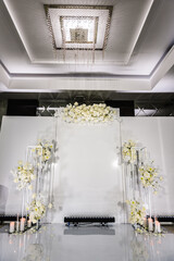 Wedding reception for luxury ceremony. Copy space. Celebration baptism concept. Photo-wall, arch place decorated candles and flowers. Trendy decor for birthday party in the banquet area.