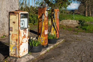 A group of three rusty and disused petrol pumps by the side of a minor road in Wiltshire, UK