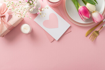 Minimalist Mother's day table arrangement. Top view flat lay of plates, cutlery, tulips, gift box, greeting card on pastel pink background with space for promotional text or advert