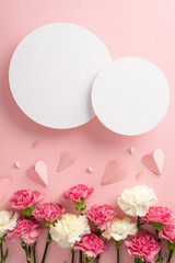 Mother's Day concept. Top vertical view flat lay of elegant carnation flowers, and pink paper hearts on a soft pastel pink background with two blank hearts for advert