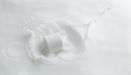 Cosmetic container white lotion droplet fly splashing. Milk lotion pour float to cosmetic bottle. Moisturizer lotion explosion spill. White background isolated high speed shutter freeze top view