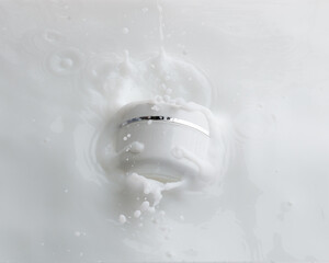 Cosmetic container white lotion droplet fly splashing. Milk lotion pour float to cosmetic bottle. Moisturizer lotion explosion spill. White background isolated high speed shutter freeze top view