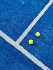 Vertical top view of two green balls on a blue artificial grass paddle tennis court by white line