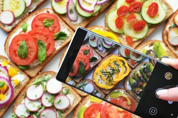 Social media influencer taking photo with smartphone of food, vegetable sandwiches, to post online.