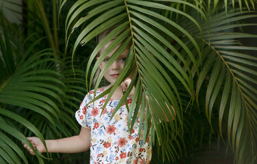 Candid outdoor portrait of adorable 5 years old girl between palm leaves, tropical vacation concept