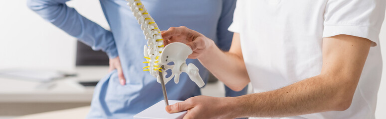 partial view of physiotherapist showing spine model to patient in rehab center, banner.