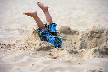 Child has fallen in a pit on the beach, only his legs are seen  - obrazy, fototapety, plakaty