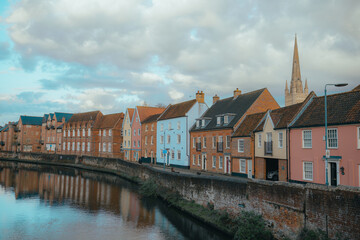 Fototapeta na wymiar Norwich riverside houses, River Wensum in Norwich, Norfolk, United Kingdom city townhouses, colourful house blue, pink, cathedral church spire, rural location