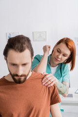 physiotherapist examining injured shoulder of bearded man in rehabilitation center.