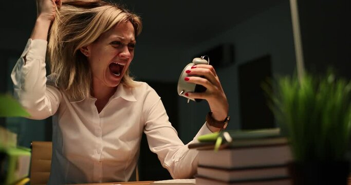 Frightened businesswoman looking at time on alarm clock and screaming at office desk late at night during thunderstorm 4k movie. Stay late at work and miss last bus concept