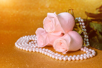 Pink rose and pearl necklace on a shiny gold background