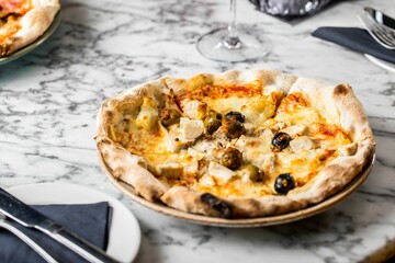 Closeup of a pizza on the tablecloth, a napkin with knife and fork near