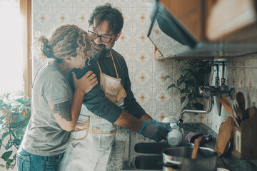 One man helping wife in housework job washing the dishes in the kitchen. Woman appreciate husband help in housekeeping leisure activity. Couple smile and hug with love inside home cleaning together