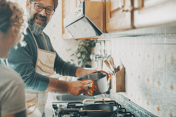 Real couple cooking together at home in the kitchen. One man smile to a woman and using pots preparing lunch. Husband and wife living in apartment. Mature people in indoor leisure activity happiness