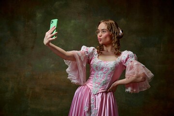 Portrait of beautiful blond princess wearing fancy pink dress and doing selfie on tablet over vintage texture background. Duck lips selfie © Lustre Art Group 