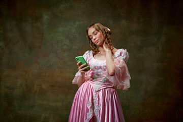 Portrait of beautiful blond princess wearing fancy pink dress and taking photo on cell phone over vintage texture background. Typical girl