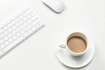 White cup of coffee next to a keyboard and computer mouse
