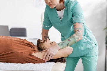 Obraz na płótnie Canvas tattooed physiotherapist massaging painful arm of bearded man during treatment in rehabilitation center.