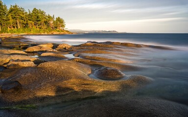 Long exposure shot of sea waves from a rocky shore with beautiful hills and trees in the background