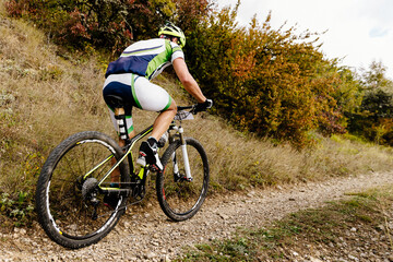 male cyclist riding mountain bicycle on gravel road with bushes on side in cross-country cycling competition