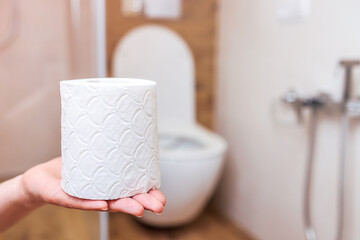 woman's hand tears off roll of white toilet paper close-up. bathroom background