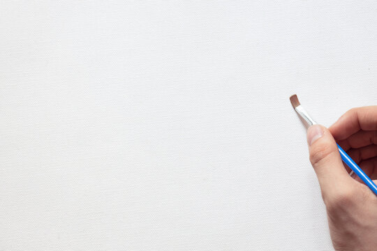 hand of the artist with a brush on the background of a white canvas, a blank sheet for creativity, free space