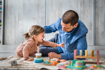 Obraz premium One man caucasian playing at home with his daughter toddler on the floor with wooden toys, modern parenthood lifestyle single parent concept 